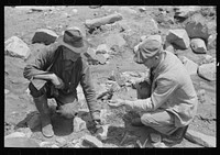 Gold prospector on the right who is working a claim down the canyon is visiting and examining ore speciman of the prospector on left. Pinos Altos, New Mexico by Russell Lee