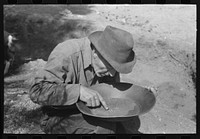 Prospector pointing to flecks of gold in his pan. Pinos Altos, New Mexico by Russell Lee