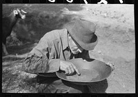[Untitled photo, possibly related to: Prospector blowing on pan of fine dirt which contains particles of gold in order to blow the dirt away and leave the heavy gold. In this dry panning the pan is rotated until the dirt is on one side and then with a decisive toss it is thrown into the air, the light dirt being then blown away by the wind and the heavy gold being caught again in the pan. Pinos Altos, New Mexico] by Russell Lee