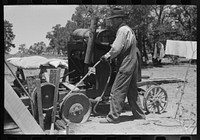 Farmer drilling water well. In this picture he is loosening and tightening rope around the pulley, thus raising and lowering the drilling tool. Pie Town, New Mexico by Russell Lee