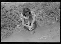 Spanish-American woman washing in irrigation ditch, Chamisal, New Mexico by Russell Lee