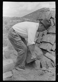 Removing the rough edges from adobe bricks with a trowel, Penasco, New Mexico by Russell Lee