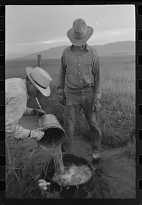 Mr. Eddie Cruzen (with cigarette holder) and ranch hand mix up blue vitriol for treating hoof rot, Cruzen Ranch, Valley County, Idaho by Russell Lee