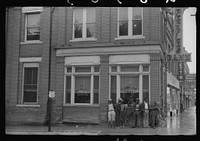 es standing on the corner of the main street on rainy Memorial Day. Roxboro, North Carolina. Sourced from the Library of Congress.