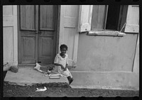 [Untitled photo, possibly related to: Little girl playing with her Christmas presents on a side street in Charlotte Amalie, Virgin Islands]. Sourced from the Library of Congress.