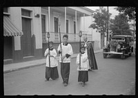 A funeral procession along the main street in Yauco, Puerto Rico. Sourced from the Library of Congress.
