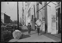 Cotton "snake," waste cotton on sidewalk and cotton samples being carried to sampling and classing rooms in broker's office on Cotton Row, Front Street, Memphis, Tennessee. Sourced from the Library of Congress.
