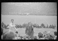 Kay Kyser and cheerleader cheering for North Carolina team at Duke University-North Carolina football game. Durham, North Carolina. Sourced from the Library of Congress.