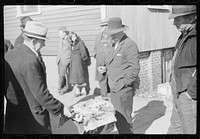 [Untitled photo, possibly related to: Salesman displaying patent medicine to farmers who have brought tobacco to warehouse and are waiting outside for the sales to begin. Mebane, North Carolina]. Sourced from the Library of Congress.
