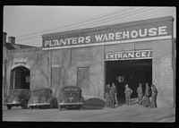 [Untitled photo, possibly related to: Farmers waiting around outside warehouse for tobacco auction sale to begin. Tobacco was brought in trailer to warehouse. Mebane, North Carolina]. Sourced from the Library of Congress.