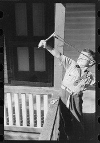 [Untitled photo, possibly related to: Mountain child shooting slingshot from porch of his home. Near Buckhorn, Kentucky]. Sourced from the Library of Congress.