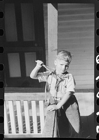 [Untitled photo, possibly related to: Mountain child shooting slingshot from porch of his home. Near Buckhorn, Kentucky]. Sourced from the Library of Congress.