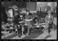 Spanish trappers and fur buyers crowd around FSA (Farm Security Administration) supervisor as he opens and reads the bids on that lot of muskrats. The auction sale is on porch of community store, St. Bernard, Louisiana. Sourced from the Library of Congress.