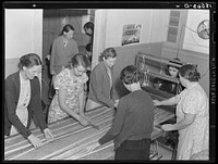 In the sewing room, migrant women are instructed in rug-making. Shafter camp for migrants (Farm Security Administration-FSA), California. Recreational, educational, cooperative activities in the camp are aided by Work Projects Administration instructors assigned to the camp programs. Sourced from the Library of Congress.