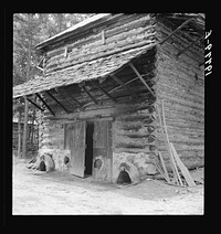 Tobacco barn with newly plastered furnace in preparation for "putting in."  Note main roof of tin and shelter roof of shingles. Person County, North Carolina. Sourced from the Library of Congress.