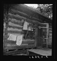 Porch on  share tenant cabin. A double one. Note the churn, lantern, baby's milk, and roof type. The other half of the cabin has a new galvanized metal roof. Near Gordonton, North Carolina. Sourced from the Library of Congress.
