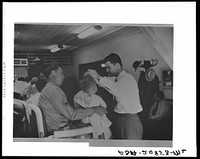 Sergeant from Fort Benning getting his son's hair cut at a barber shop in Columbus, Georgia. Sourced from the Library of Congress.