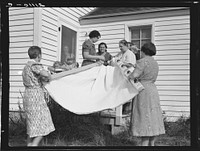 Farm women, members of the "Helping Hand" club, carefully roll up the quilt upon which they are working. Near West Carlton, Yamhill County, Oregon. General caption number 58-11 by Dorothea Lange