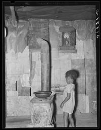 Southeast Missouri Farms. Child of sharecropper reaching for pan on stove in living room at shack home by Russell Lee