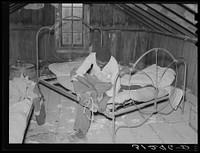 New Madrid County, Missouri. Son of sharecropper putting on shoes in attic bedroom of his home by Russell Lee