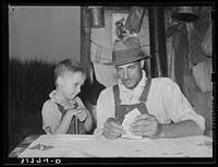 Day laborer with son playing penny-ante poker. He is a worker in the cane fields near New Iberia, Louisiana by Russell Lee