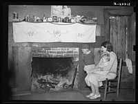Mrs. Bagget and two children in front of fireplace. Note the board window. Laurel, Mississippi by Russell Lee