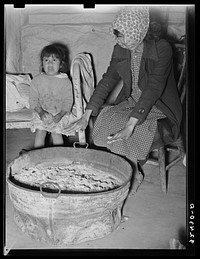 Mexican mother and child. Fires built in old galvanized tubs are used both for heat and cooking throughout the Mexican section. Crystal City, Texas by Russell Lee