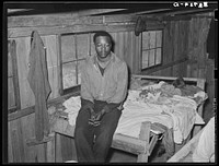  strawberry worker sitting on end of bunk in bunkhouse. Hammond, Louisiana by Russell Lee