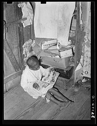  boy looking at mailorder catalogue. This house is one of those provided for migrant strawberry pickers. Near Independence, Louisiana by Russell Lee