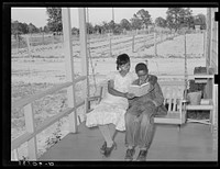 [Untitled photo, possibly related to: Wife of FSA (Farm Security Administration) client reading book to her son on swing on her front porch. Notice garden in background and title of book. Sabine Farms, Marshall, Texas] by Russell Lee