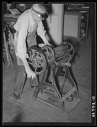 Removing excess moisture from leather by means of rollers. Leather must be moistened and tempered before being used and then excess liquid is pressed out. Bootmaking shop, Alpine Texas by Russell Lee