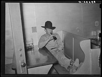 Cowboy drinking a bottle of beer in booth of beer parlor. Alpine, Texas by Russell Lee