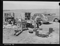 Camp cook at work with chuck wagon in center and truck for carrying bed rolls at left. Cattle ranch near Marfa, Texas by Russell Lee