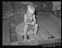 Son of agricultural day laborer examining cotton seed on front porch of home. Muskogee County, Oklahoma by Russell Lee