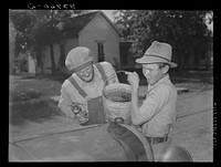 [Untitled photo, possibly related to: Pouring water into radiator of migrant's car in the streets of Muskogee, where family has stopped to say goodbye to their friends in that town. Oklahoma] by Russell Lee
