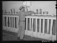 Attendant dumping bucketfull of cattle ration into feed stalls for cows to eat while being milked. Dairy, Tom Green County, Texas by Russell Lee