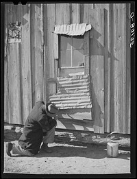 Pomp Hall,  tenant farmer, repairing piece of tin which covers window of his house. Creek County, Oklahoma by Russell Lee