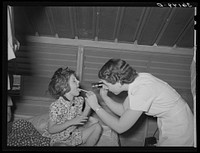 Nurse examining child of migratory laborer in family metal shelter at the Agua Fria migratory labor camp. Arizona by Russell Lee