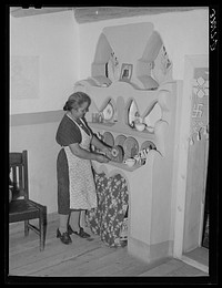 Wife of Spanish-American family arranging things in adobe cupboard which she designed and built. Chamisal, New Mexico by Russell Lee