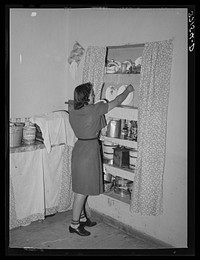 Daughter of Spanish-American putting dishes into cupboard. Chamisal, New Mexico by Russell Lee