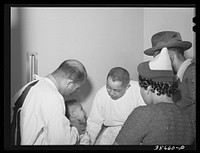 Doctors examining baby whose parents have just brought him into the clinic at the  hospital. Chicago, Illinois by Russell Lee