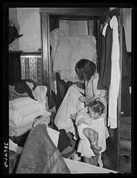 Corner of bedroom with  housewife examining bed clothing chewed by rats. Chicago, Illinois by Russell Lee