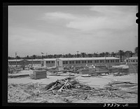 Working on jigs, with dormitories in the background at the FSA (Farm Security Administration trailer camp for defense workers. The dormitories at this project will accomodate, when finished, 952 single men. Dormitory residents will pay five dollars weekly for single rooms and three dollars and fifty cents weekly for each occupant sharing a double room. San Diego, California by Russell Lee