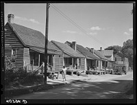 A street in the  quarter of Elizabeth City, North Carolina, where many of the migrants find lodging. In the background is one of the trucks that take them to and from work. Sourced from the Library of Congress.