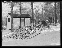 Mrs. M. Lane, young wife of a shipyard worker, gathering some wood just outside her one-room shack. The shack and little privy were built for them by her father. Made of celetex board. Bath, Maine. Sourced from the Library of Congress.