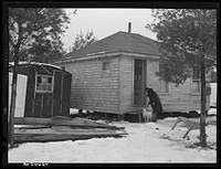 Mrs. Carol Porter setting out milk bottle. Shot shows small shack the Porters lived in while they were building their house. Sourced from the Library of Congress.