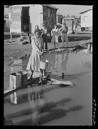[Untitled photo, possibly related to: San Juan, Puerto Rico. Fetching water from a spigot which services many people who live in the huge slum area known as "El Fangitto" ("the mud")]. Sourced from the Library of Congress.