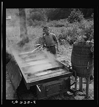 Sugarcane juice drains from barrel into vat, is boiled into molasses as it runs through to last section. Racine, West Virginia. Sourced from the Library of Congress.