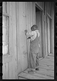 Child of former sharecropper, playing primitive musical instrument made by stretching wire from one nail to another creating sort of violin. Southeast Missouri Farms by Russell Lee