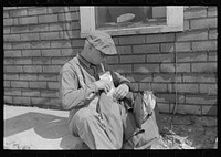 Transient putting timetable into coat pocket. Note that label of coat reads New York. Sikeston, Missouri by Russell Lee